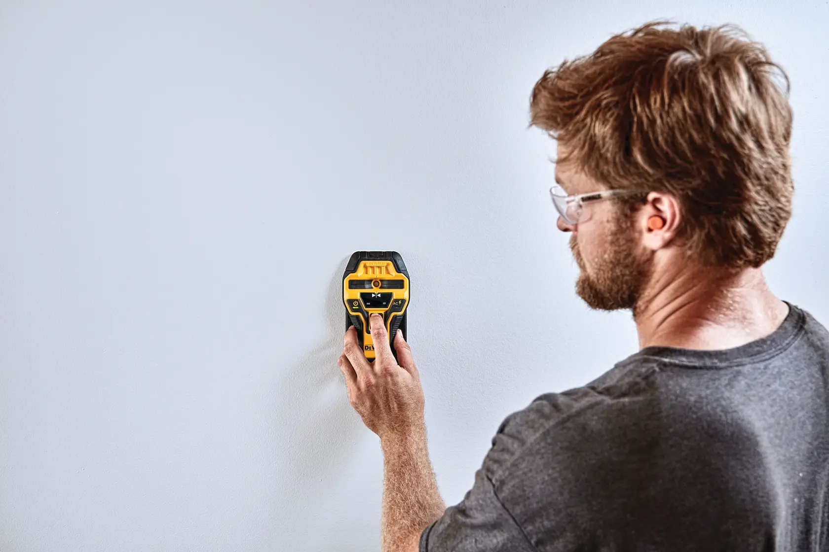 A person is using a DEWALT electronic wall scanner (model DW0350) to scan a white wall.