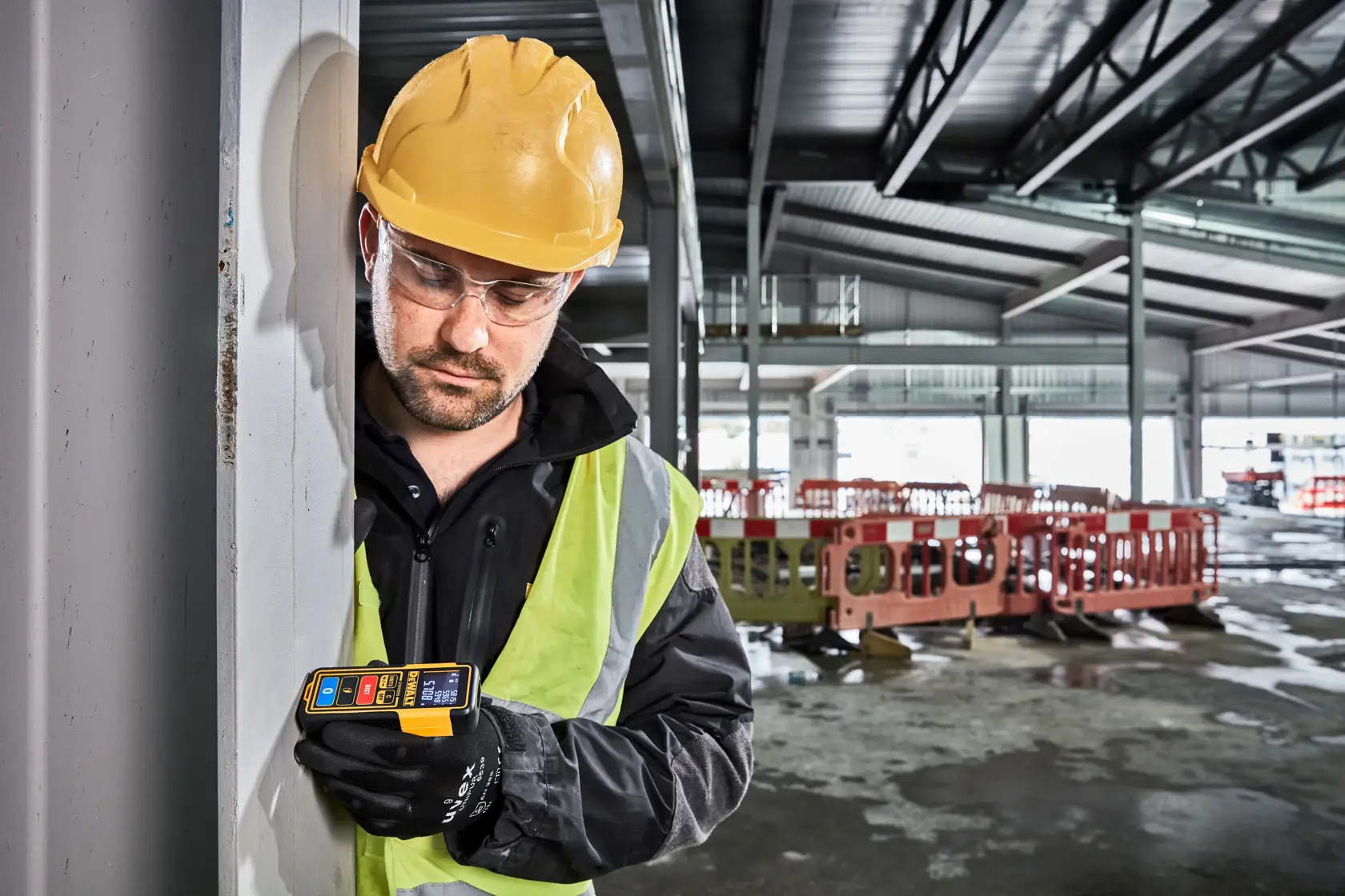 Front view of a DEWALT DW099S laser distance measurer with a digital display showing measurement readings. The device has several buttons labeled UNITS, DIST, and a Bluetooth symbol, and is predominantly yellow and black with red and blue accents.