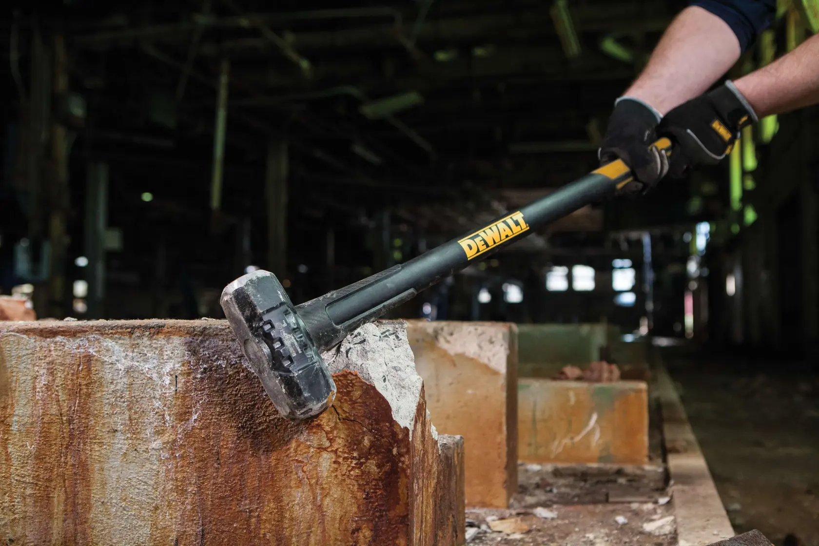 Una persona sta usando una mazza DEWALT per rompere un blocco di cemento in un ambiente industriale.