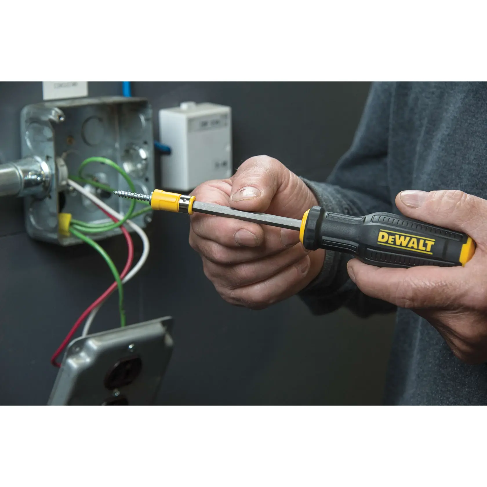 A person is using a DEWALT screwdriver to work on wiring in an electrical junction box.