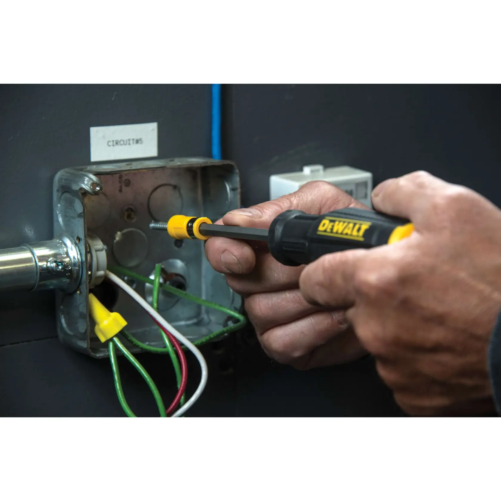 Close-up of a person using a DEWALT screwdriver to work on electrical wiring inside a metal electrical box.