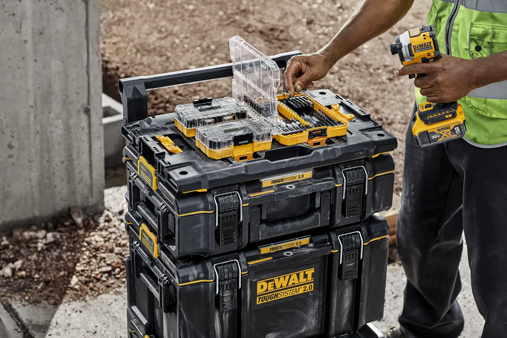 Une personne sur un chantier organise des embouts de perceuse et des accessoires sur des boîtes à outils empilées DEWALT ToughSystem 2.0, en utilisant un outil électrique DEWALT.
